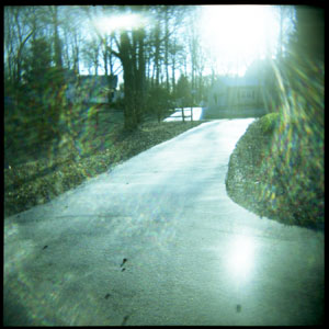 The sun rises through the trees over a wintry driveway